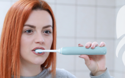 ragazza con capelli rossi che lava i denti allo specchio con spazzolino elettrico